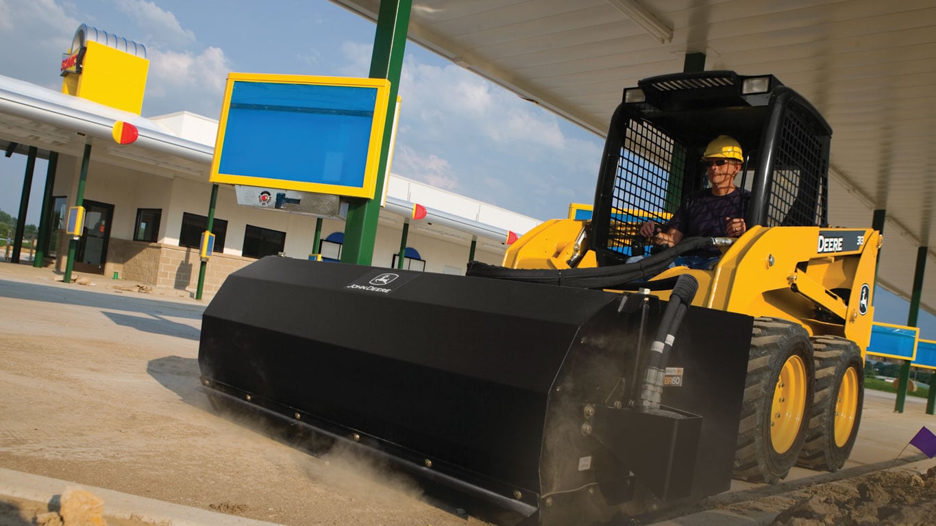 John Deere Skid Steer with pickup broom attachment sweeping.